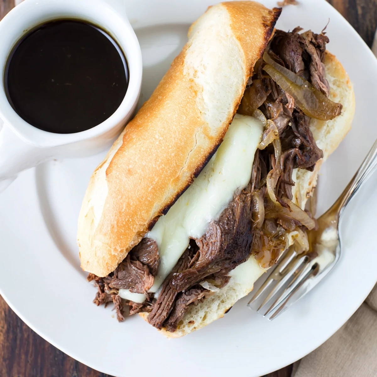 Slow cooker French Dip Sandwiches piled high with juicy beef alongside a steaming bowl of rich au jus