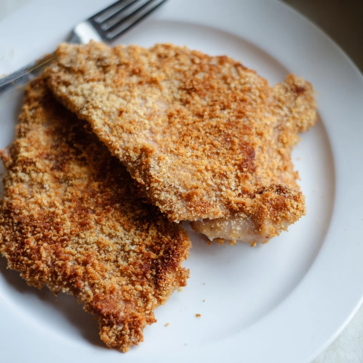 Crispy fried chicken breast resting on paper towels, golden brown breading, steam rising from surface