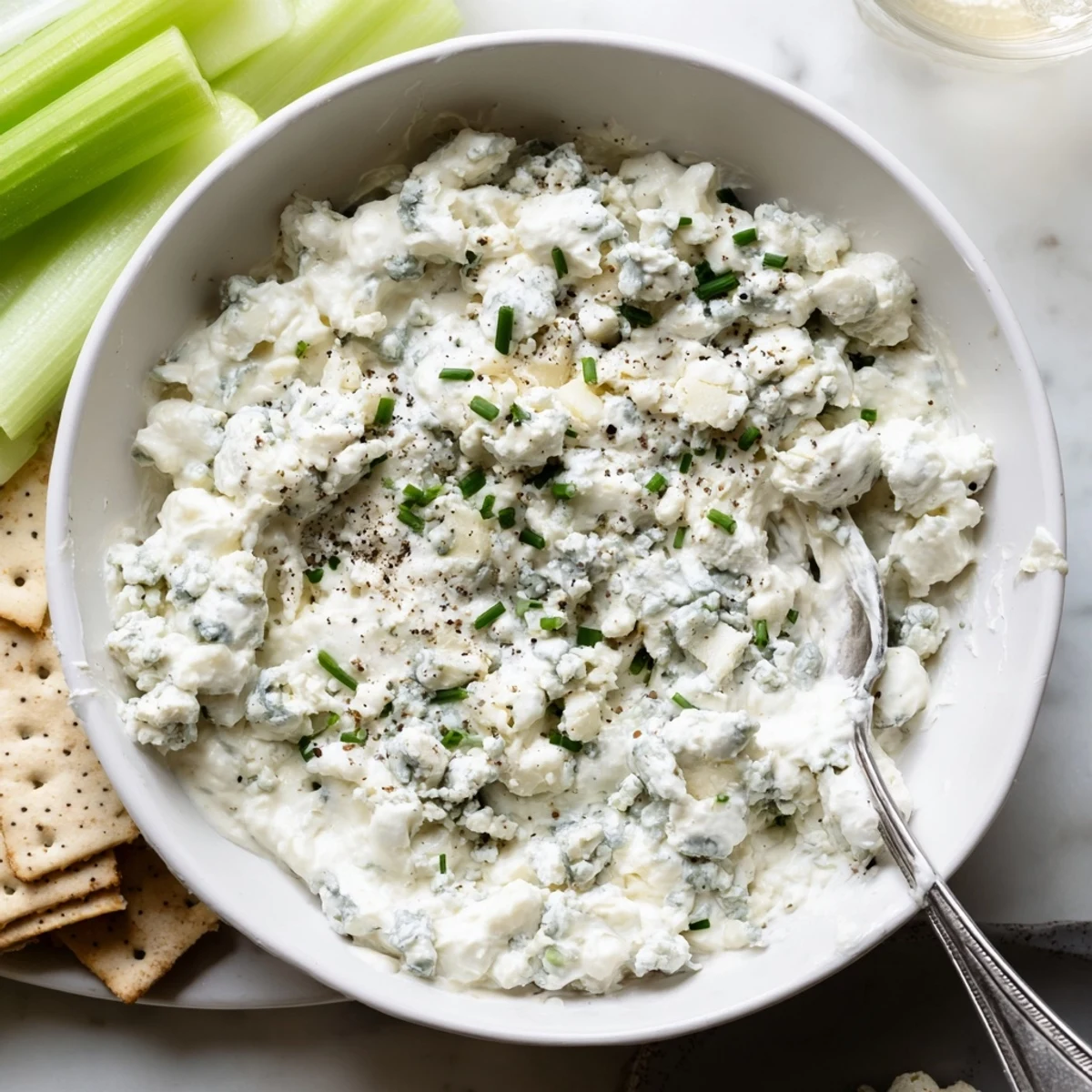 Creamy blue cheese dip served in a bowl with crisp celery sticks and crackers