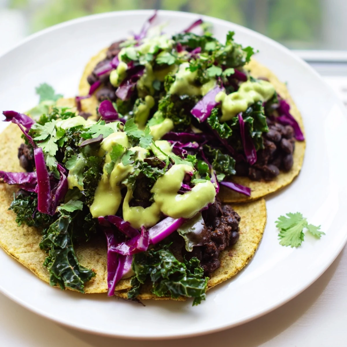 Smoky Black Bean Kale Tacos topped with sautéed greens, red cabbage, and herby avocado sauce