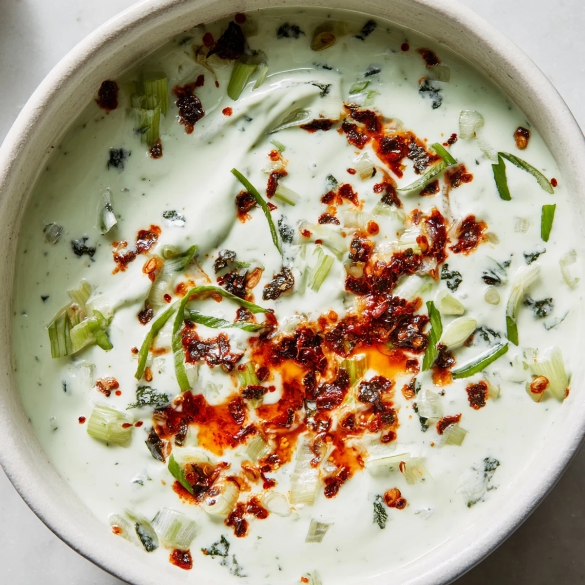 Creamy charred scallion and chili crisp dip swirled with spicy oil in a rustic bowl