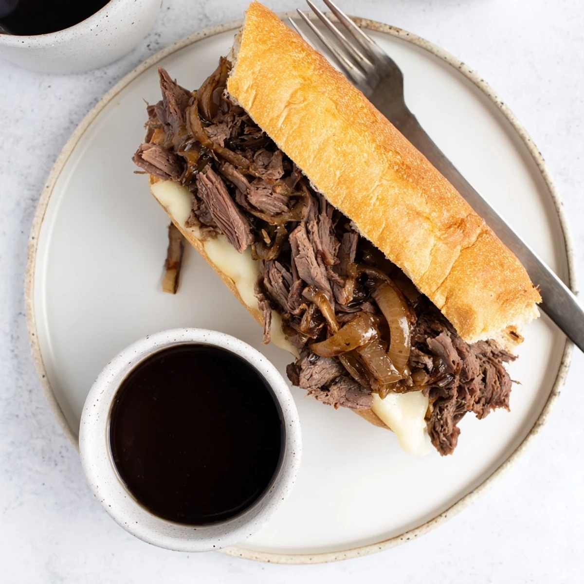 Golden Crockpot French Dip Sandwiches with melted cheese ready to dip into flavorful dark beef broth