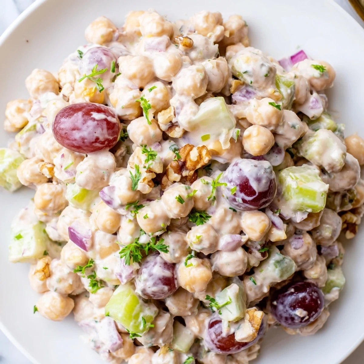 Vibrant bowl of vegan chicken salad dotted with red grapes walnuts and green herbs