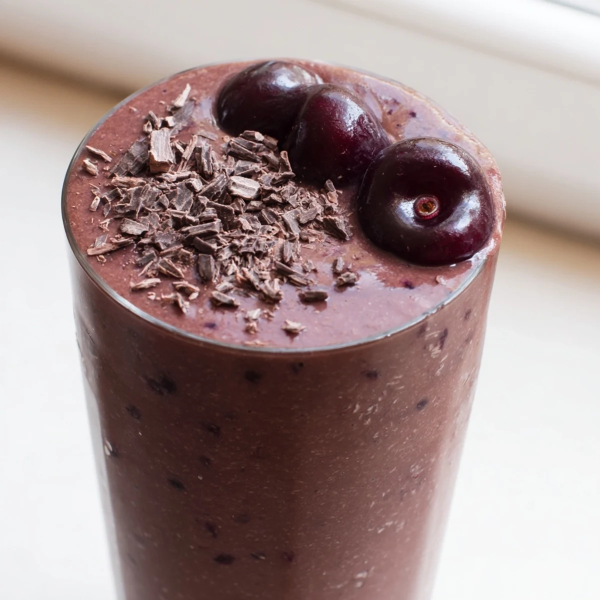 Rich chocolate cherry protein shake poured into a glass with dark chocolate shavings