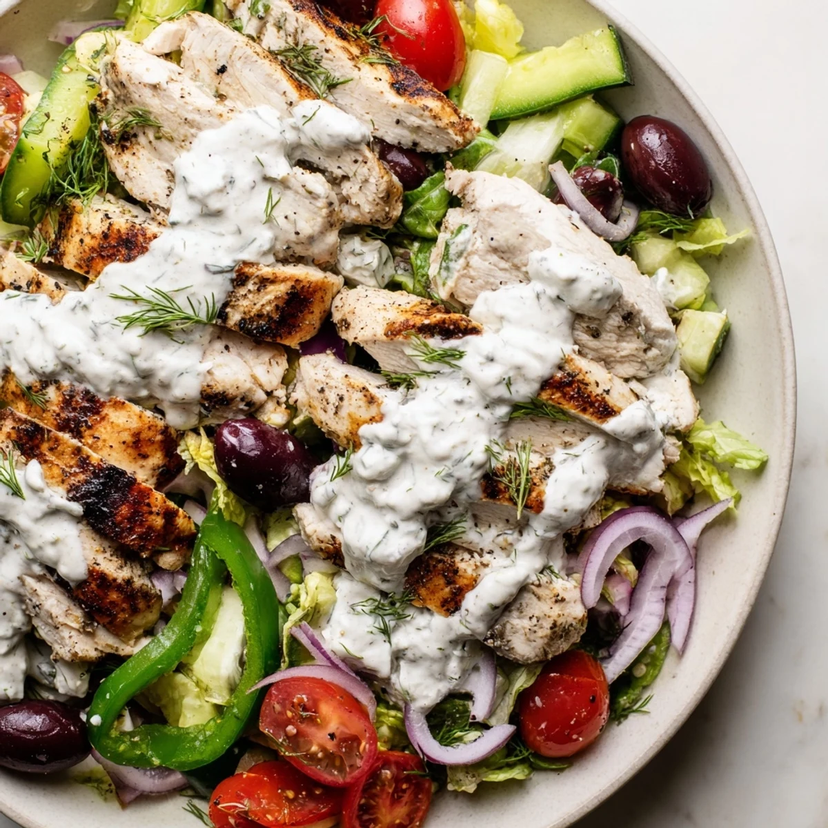 Juicy sliced grilled chicken rests atop a crisp Greek chicken salad drizzled with velvety whipped feta dressing