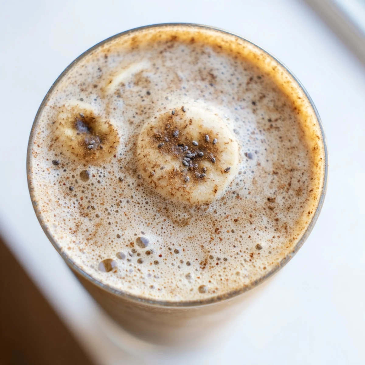 Creamy banana protein coffee smoothie topped with a frothy, golden-brown foam layer