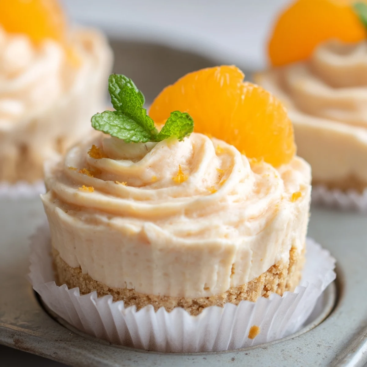 Creamy mini no bake orange cheesecakes topped with fresh orange segments and mint