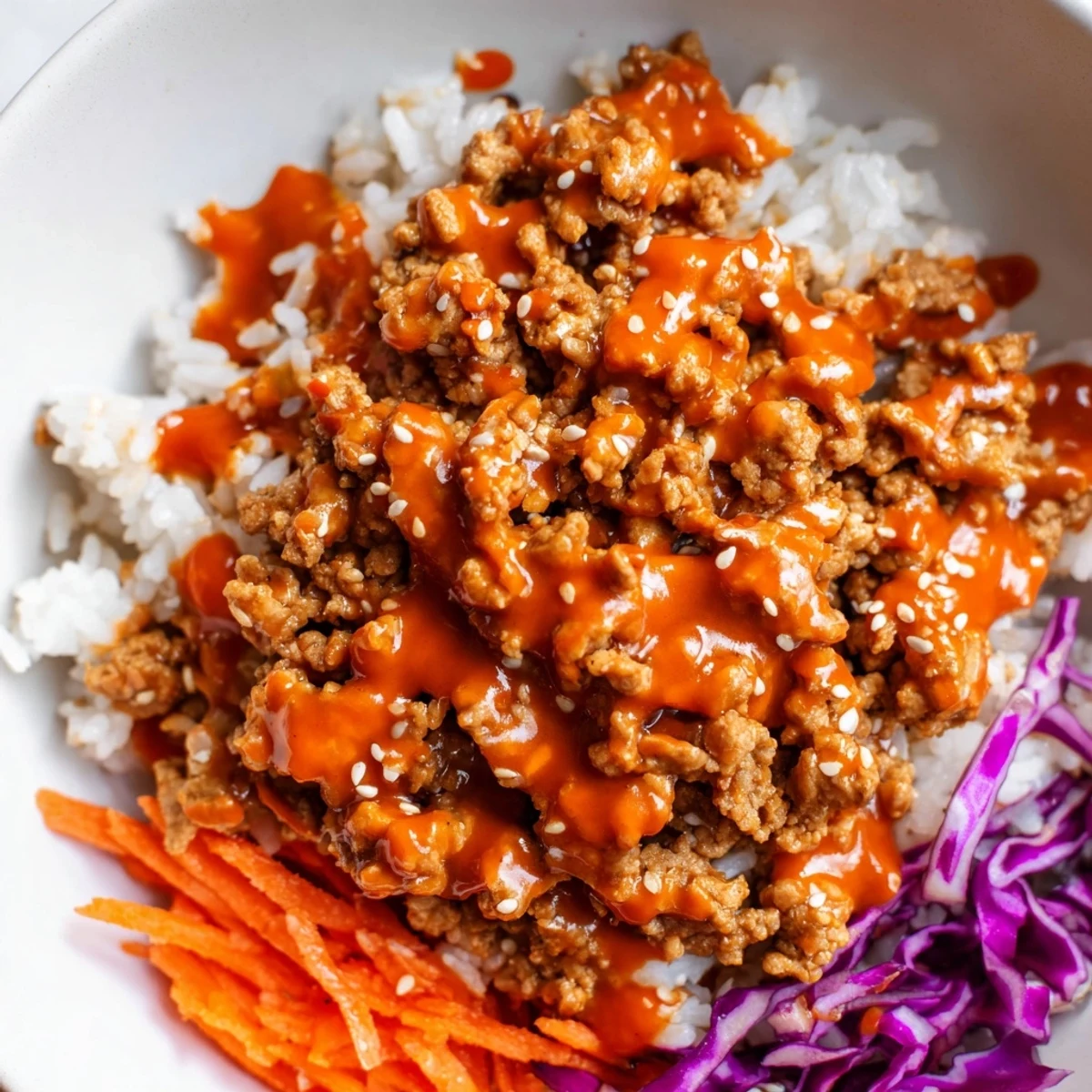 Hearty Ground Turkey Rice Bowls topped with shredded carrots, cucumber, and sweet spicy sauce