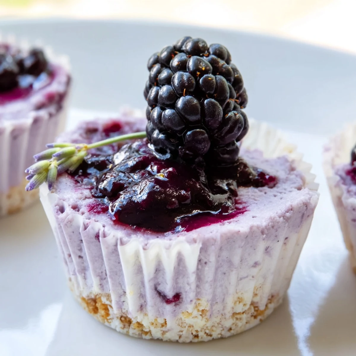 Creamy No Bake Mini Blackberry Lavender Cheesecakes topped with glossy purple berry sauce on a rustic dessert plate