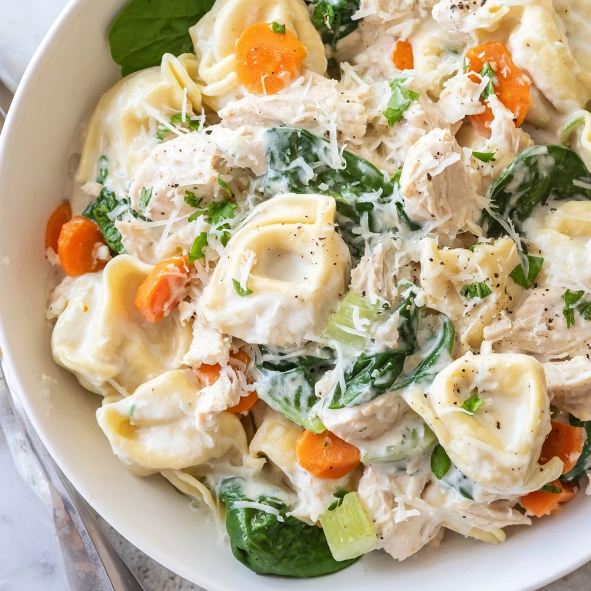 Creamy crockpot chicken tortellini topped with Parmesan in a white bowl