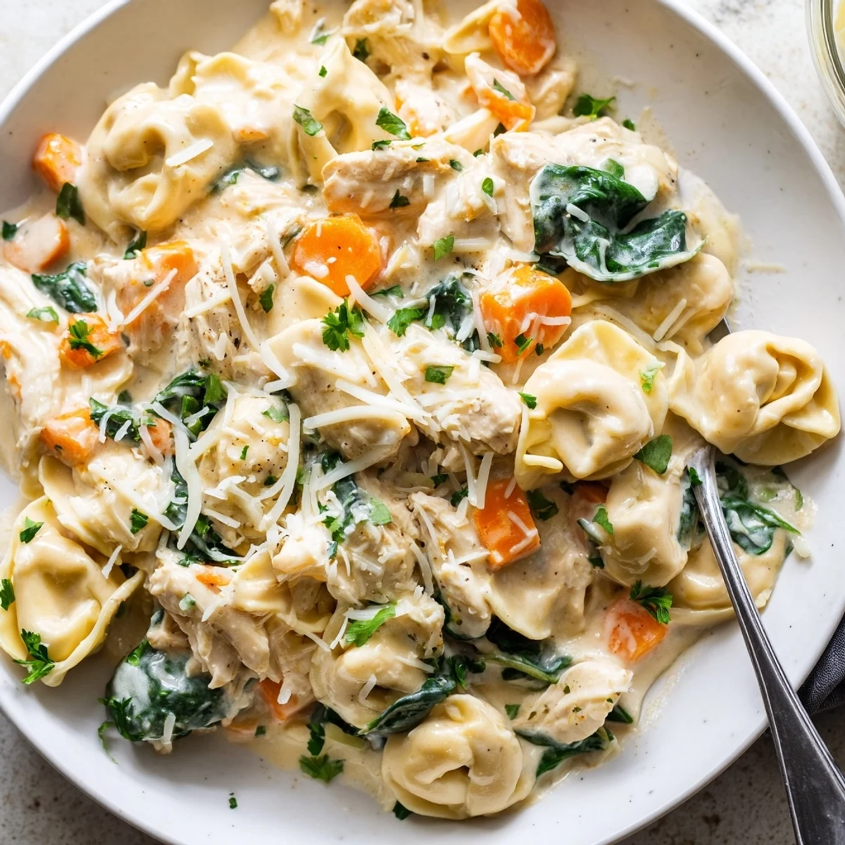 Hearty crockpot chicken tortellini with spinach and carrots served steaming on a rustic table