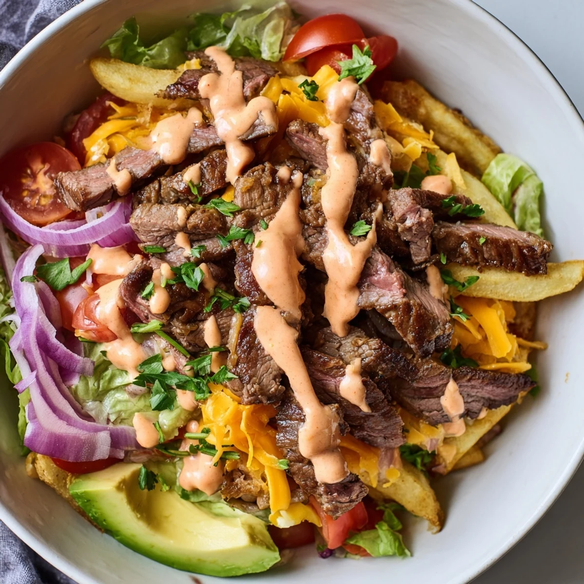 Tender seared steak strips piled over golden fries with fresh avocado slices