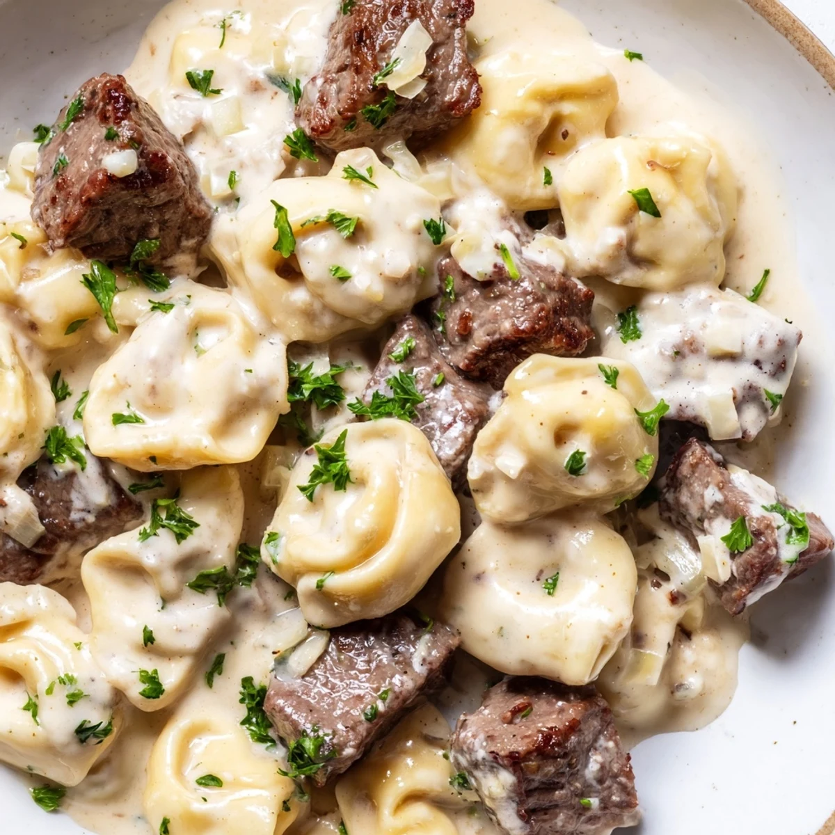 Creamy garlic steak tortellini plated in a white bowl with fresh parsley sprinkled on top