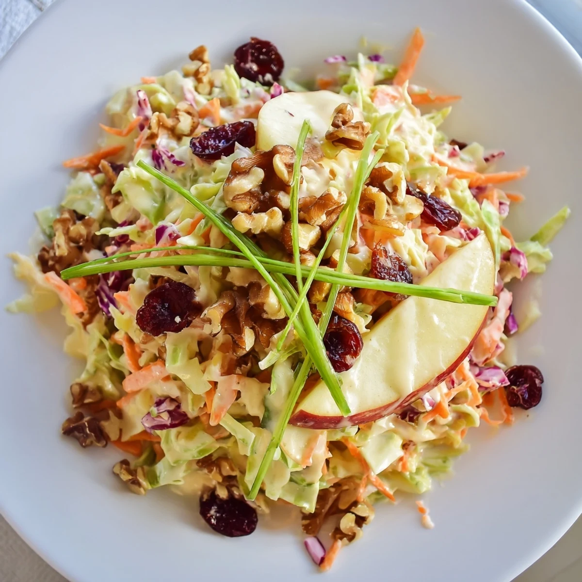 Vibrant cranberry apple coleslaw topped with walnuts and green onions in a white bowl.