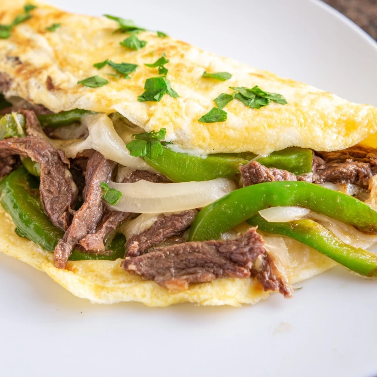 Classic Philly cheesesteak omelette topped with parsley, featuring juicy beef and melted cheese.