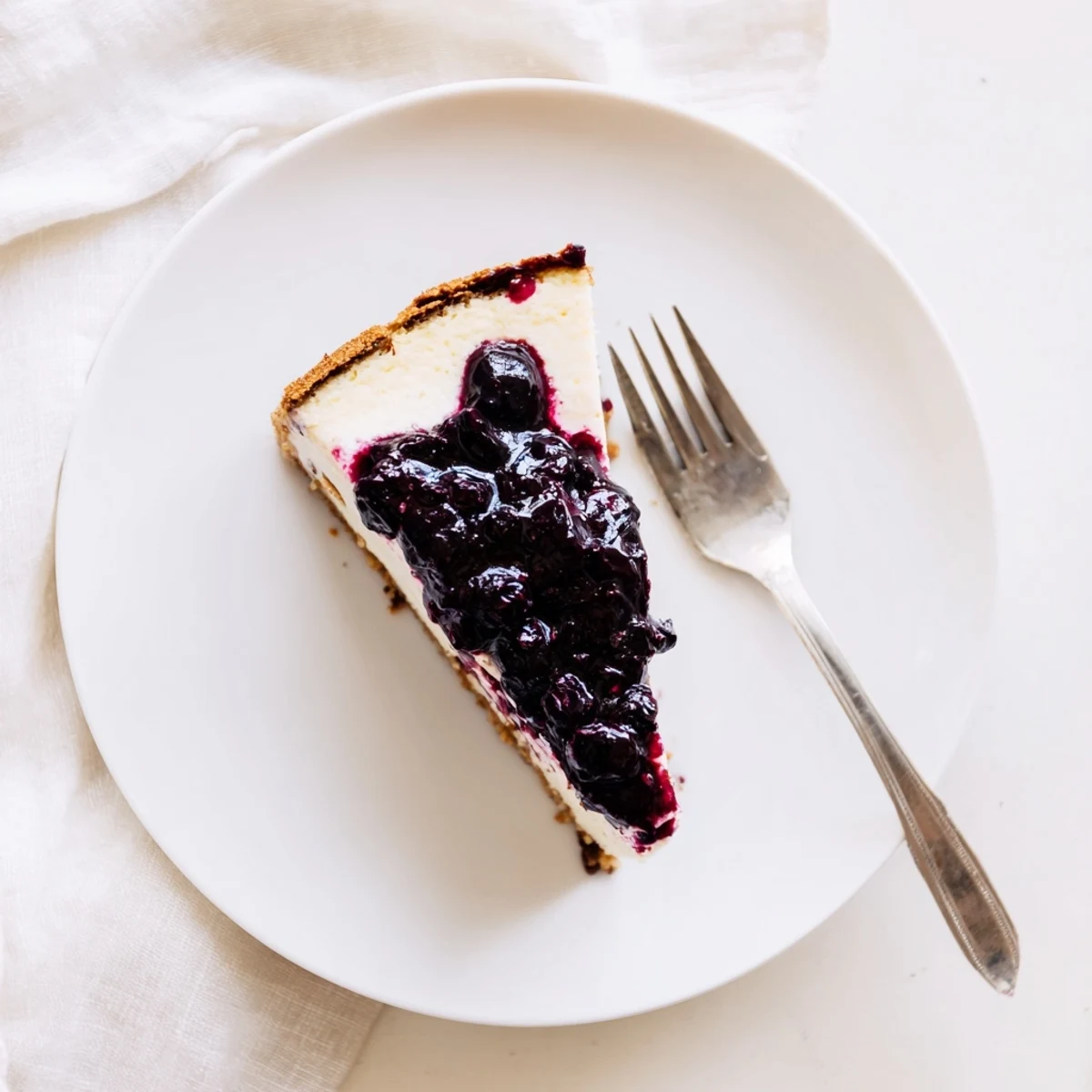 Creamy blueberry cheesecake slice topped with sweet compote on a white plate.