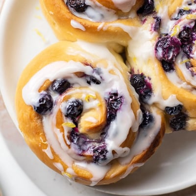 Freshly baked Lemon Blueberry Sweet Rolls with Vanilla Icing in a ceramic dish, warm and perfect for a weekend breakfast spread.