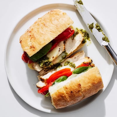 Warm chicken pesto sandwich recipe layered with fresh spinach on a golden roll.